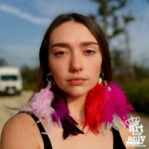 Woman wearing colorful feather earrings with a blurred outdoor background