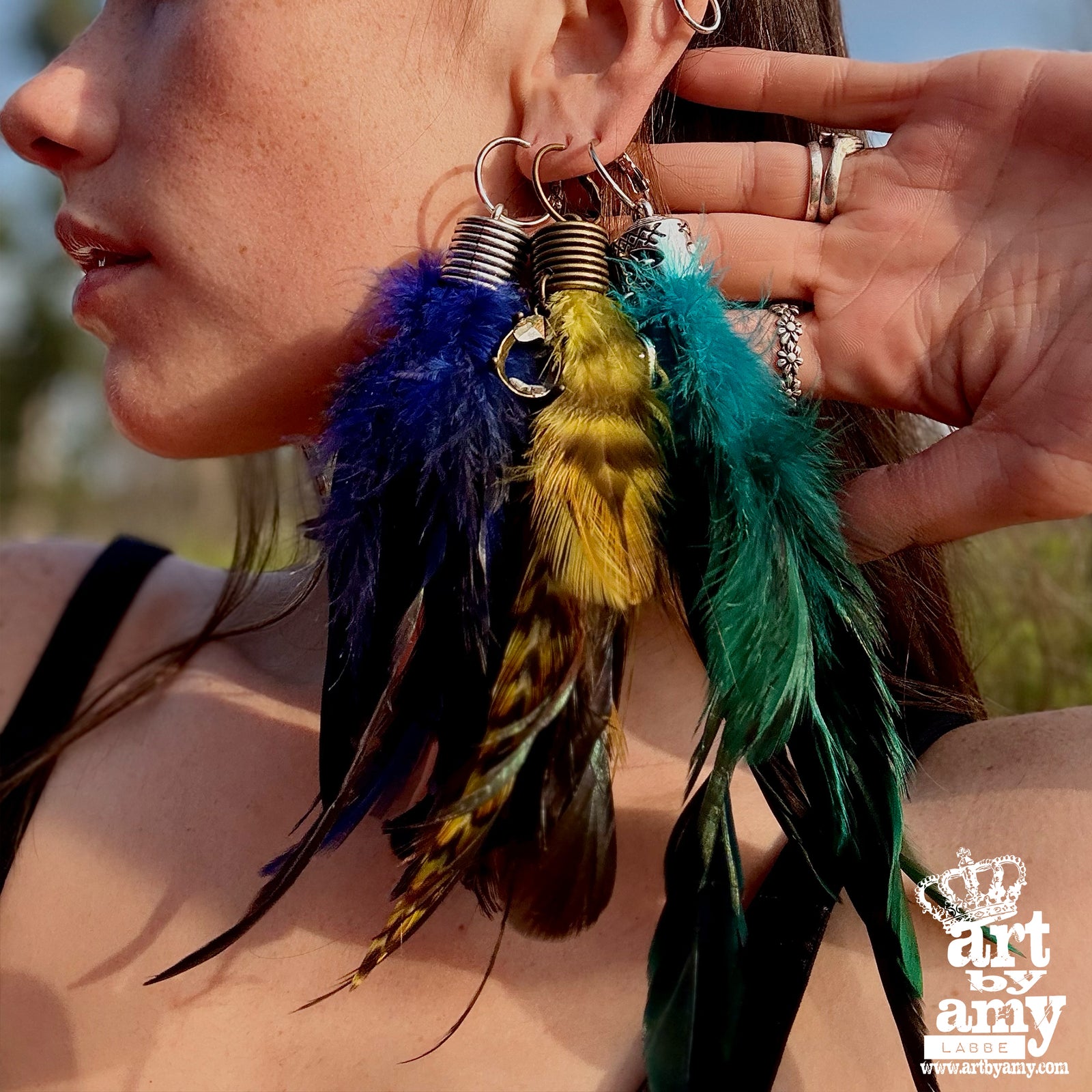 Close-up of colorful feather earrings being held by a hand with a blurred natural background