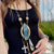 Close-up of a person wearing an ornate necklace with a blue pendant, blurred background