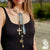 Woman wearing a long, ornate necklace with various pendants outdoors.